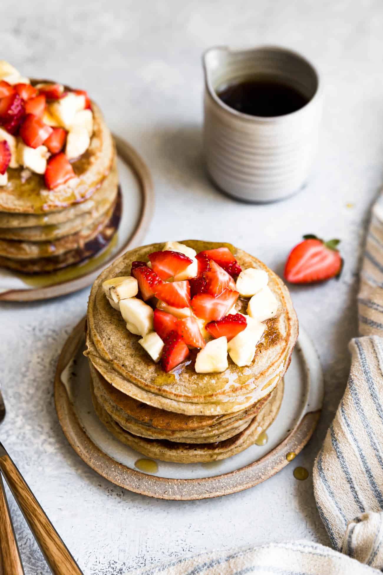 banana oatmeal pancakes on ceramic plates with strawberries, bananas and syrup