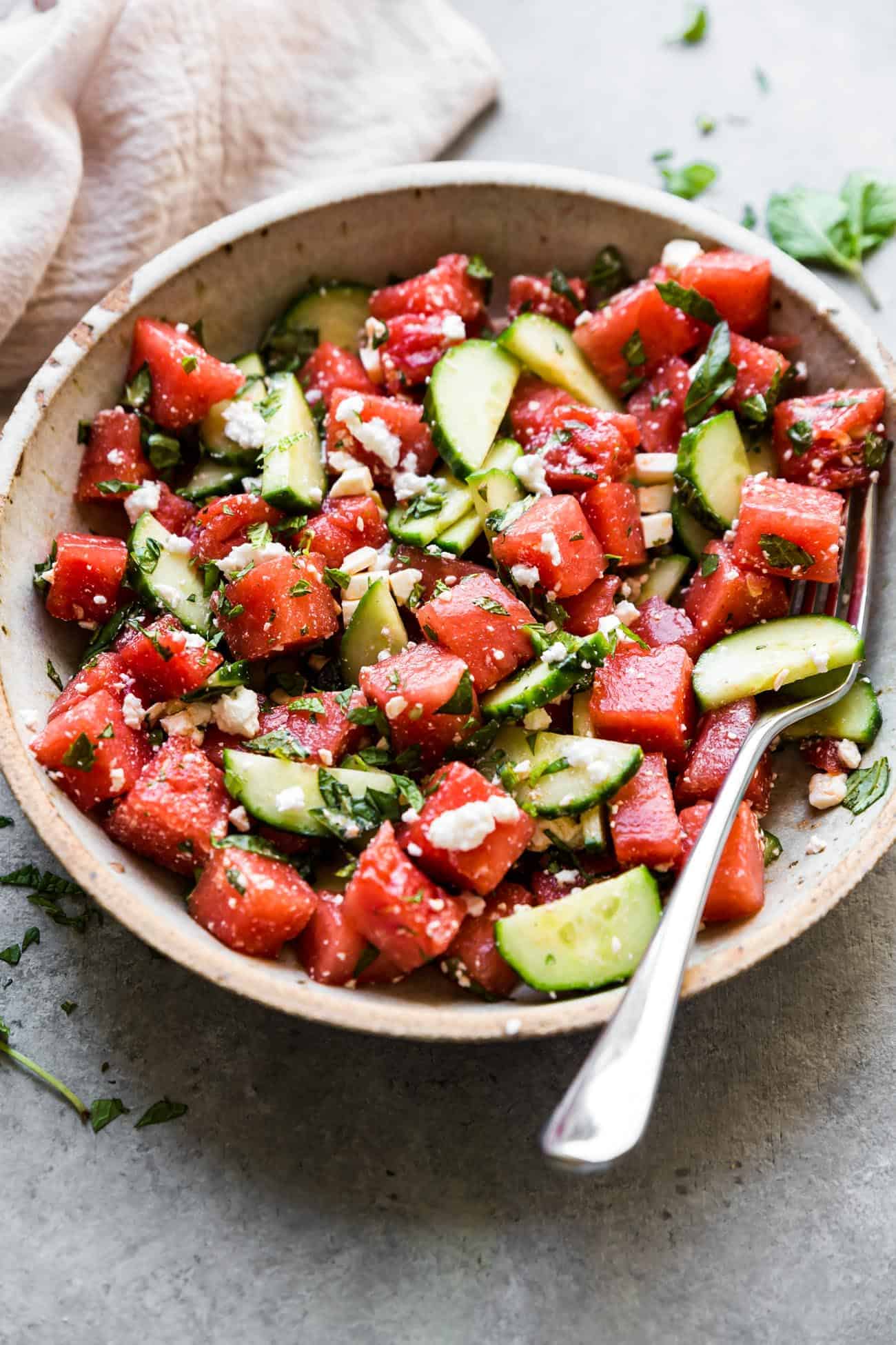 watermelon basil salad with feta in a bowl with cucumbers and a fork