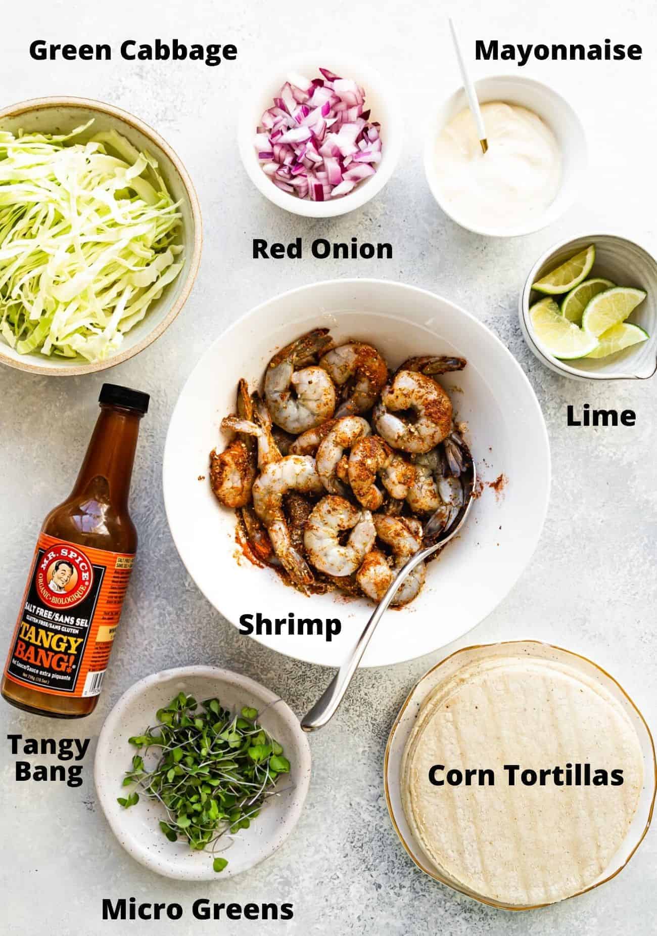 ingredients to make shrimp tacos laid out in bowls: Green cabbage, red onion, mayonnaise, lime, chrimp, tangy bang, corn tortillas