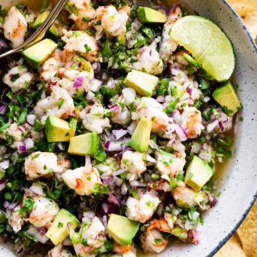 shrimp ceviche in a bowl with avocado and limes
