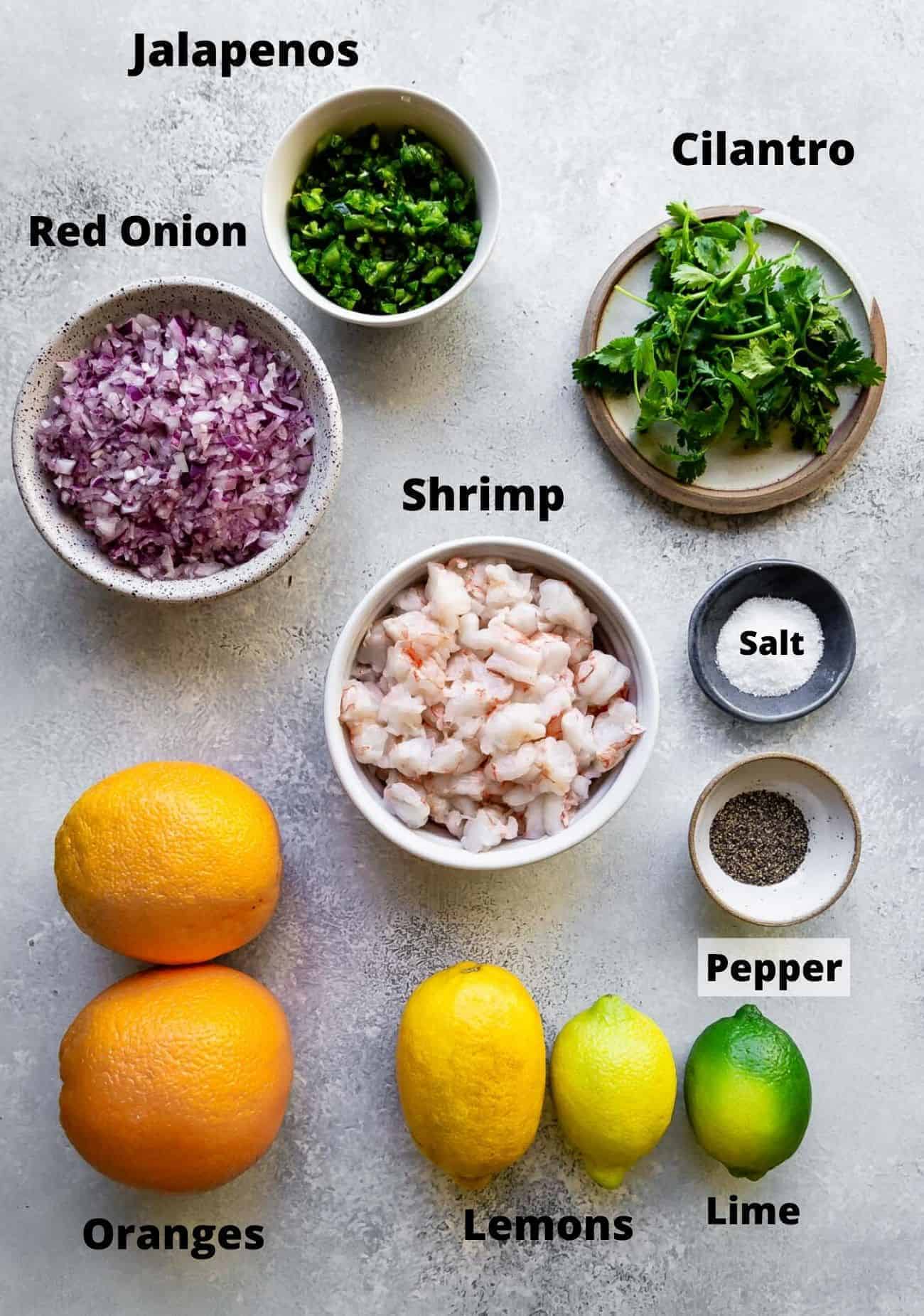 ingredients laid out to make shrimp ceviche: jalapenos, red onion, cilantro, shrimp, salt, pepper, lime, lemons, oranges