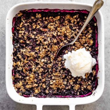 blueberry crisp in a white pan with a spoon and ice cream on top