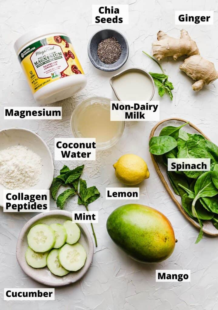 ingredients laid out to make a green pregnancy smoothie: chia seeds, ginger, magnesium, non-dairy milk, coconut water, spinach, lemon, mint, mango, collagen peptides, mango, cucumber