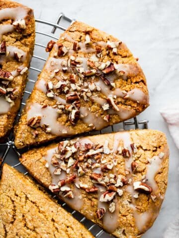 gluten free pumpkin scones on a circular wire rack with glaze and pecans