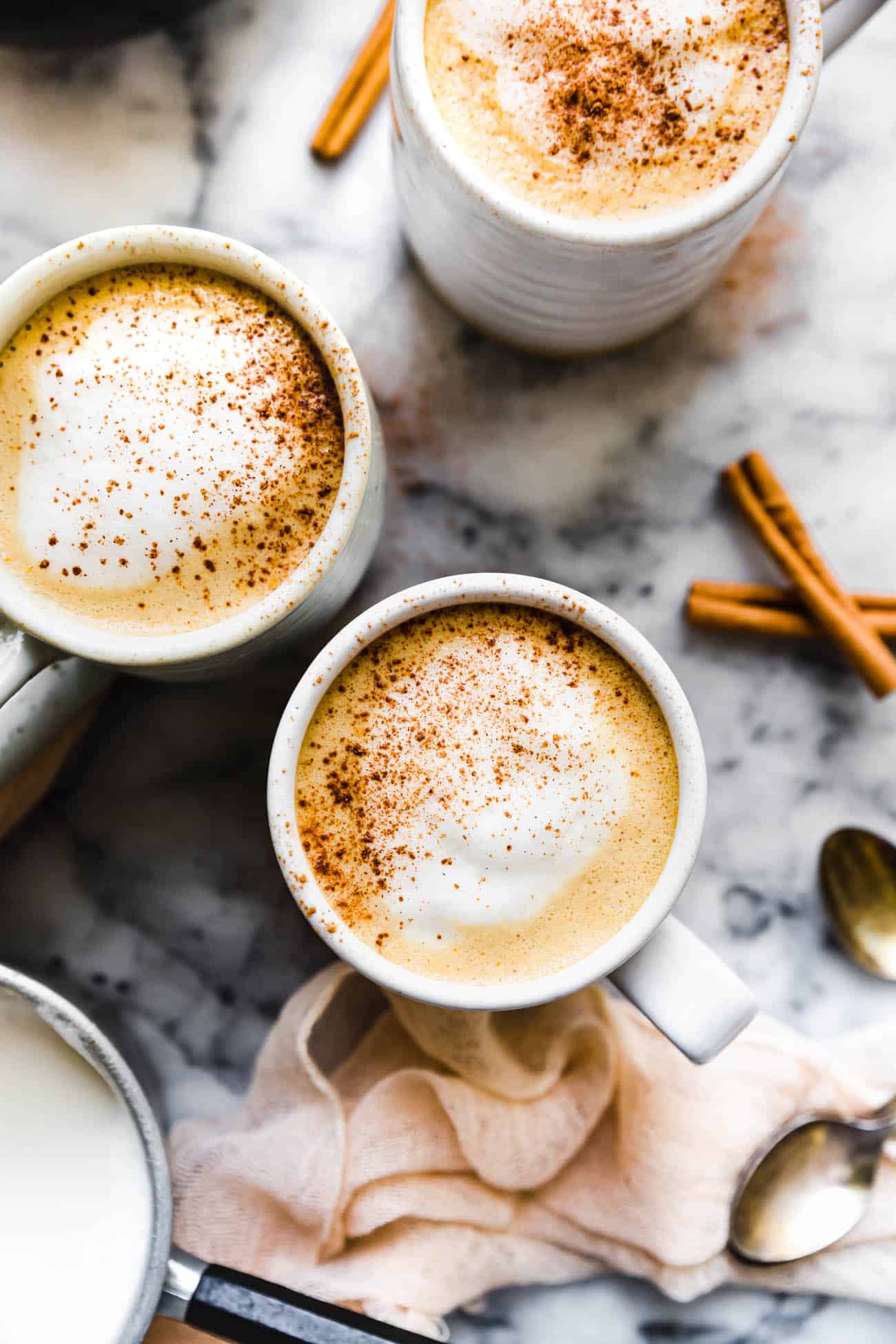 pumpkin spice lattes in mugs with foam and cinnamon on top
