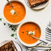 two bowls of tomato soup with grilled cheese on the side