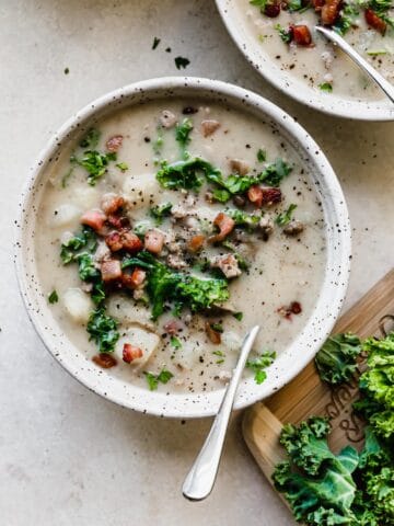 Instant Pot Zuppa Toscana in a bowl with kale on the side on a cutting board