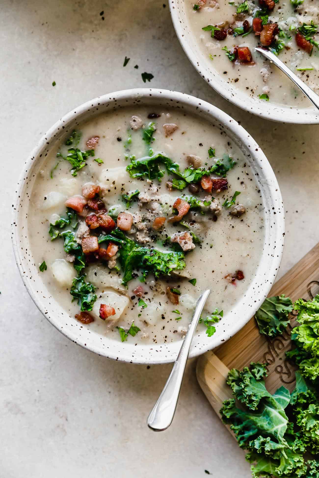 Instant Pot Zuppa Toscana in a bowl with kale on the side on a cutting board