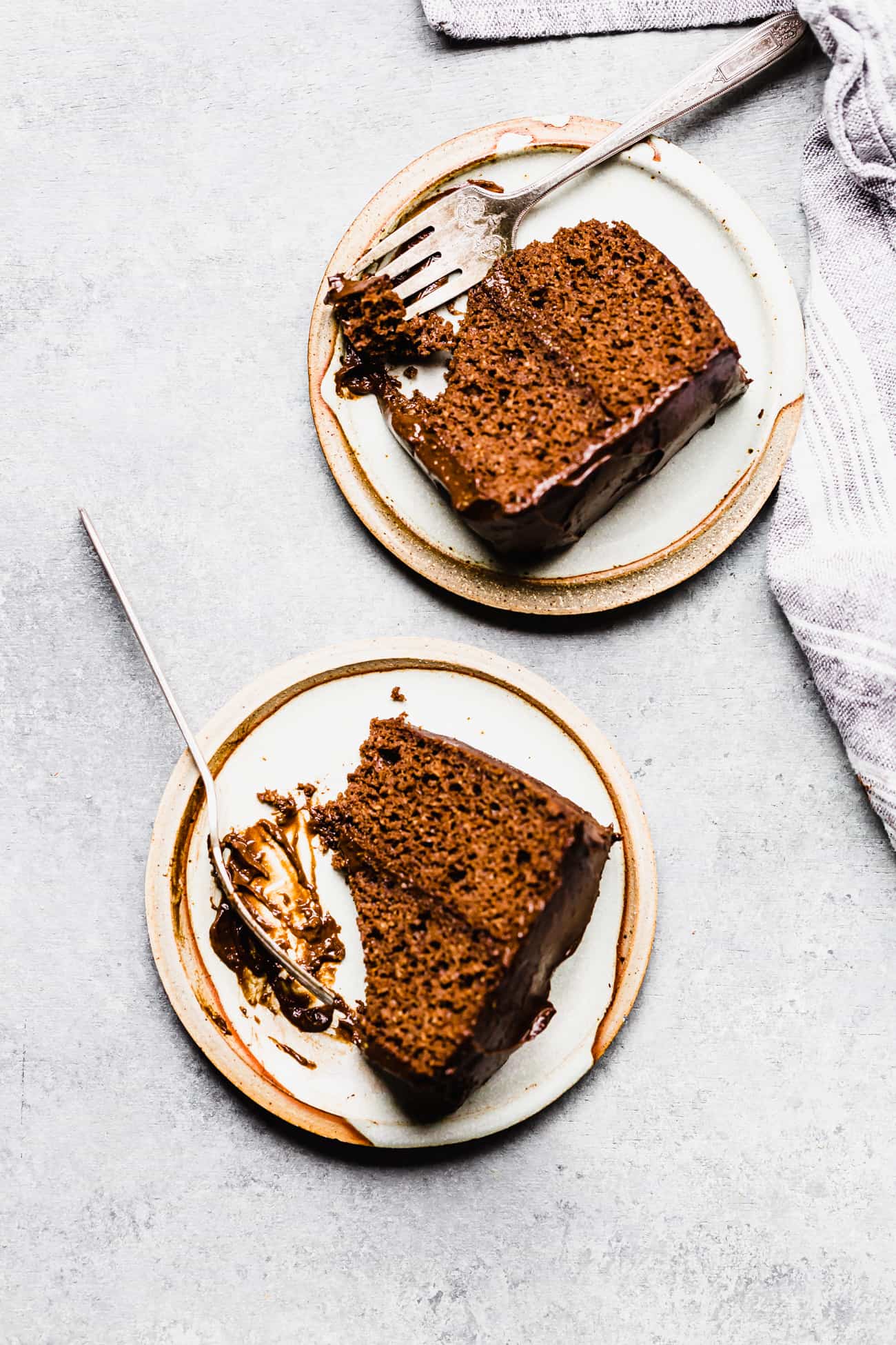 two pieces of chocolate cake on plates with forks on the side