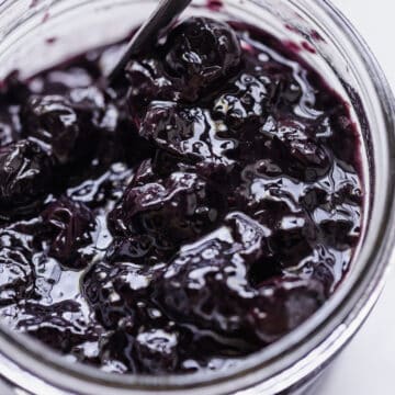 blueberry jam in a clear jar with a spoon inside