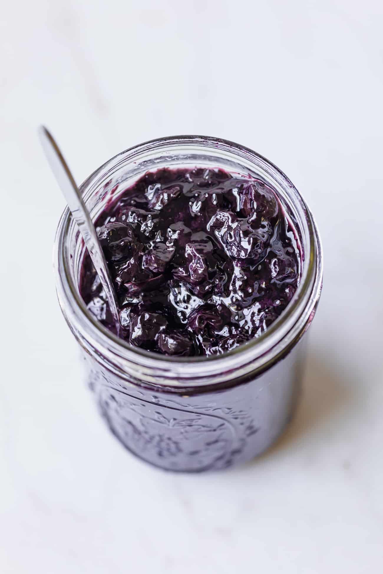 homemade blueberry jam in a glass jar with a spoon inside