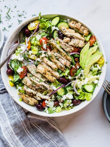Greek chicken salad in a large bowl with a metal spoon