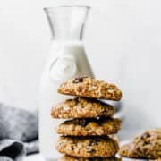 a stack of oatmeal raisin cookies with a jug of milk in the background