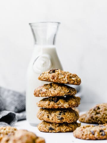 a stack of oatmeal raisin cookies with a jug of milk in the background