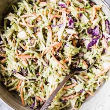 broccoli slaw in a large ceramic bowl with a serving spoon