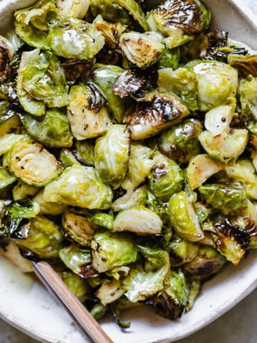 honey mustard brussels sprouts in a white ceramic bowl with a spoon inside
