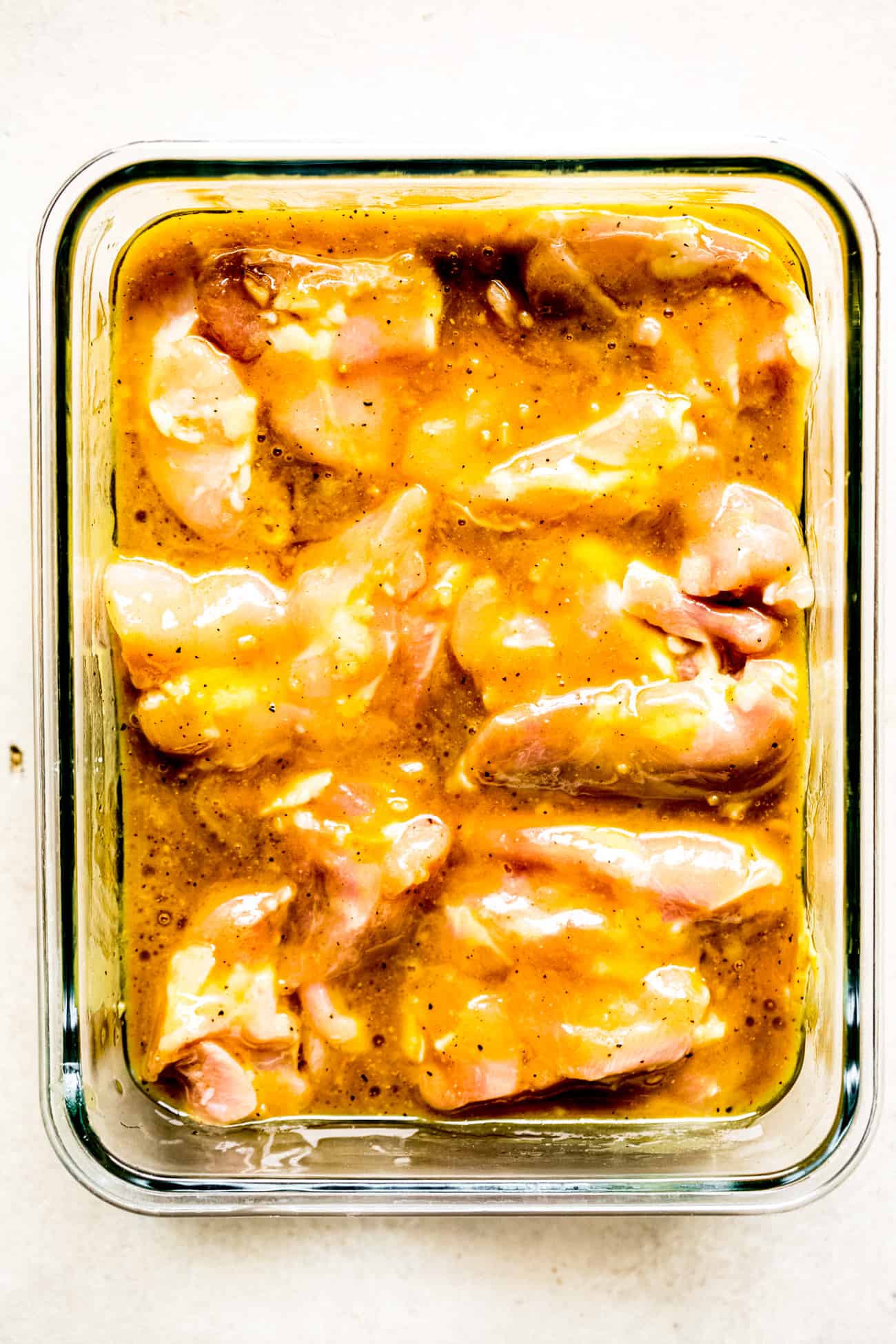chicken thighs marinating in a glass Tupperware container