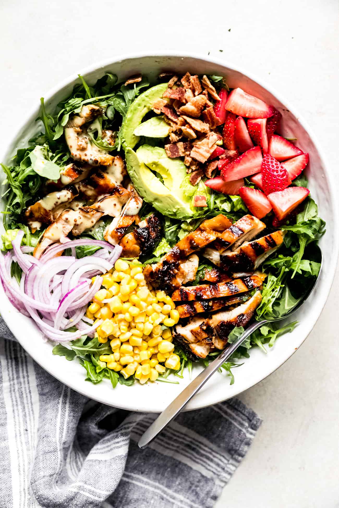 chicken salad in a large bowl with avocaod, strawberries, corn, and onions