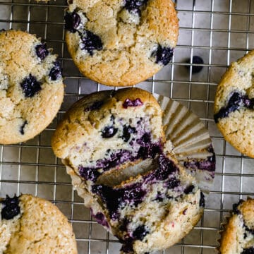 blueberry muffins on a wire rack, one cut open with blueberries on the inside and on top