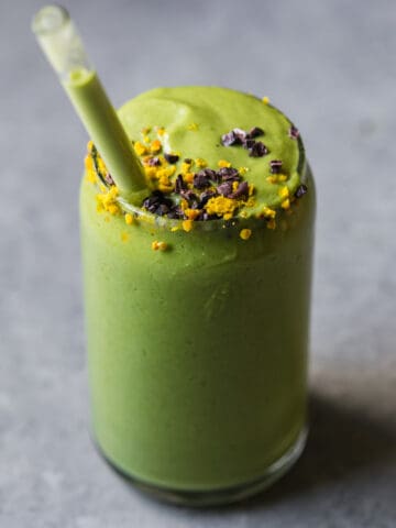 green avocado smoothie with a glass straw and bee pollen on top
