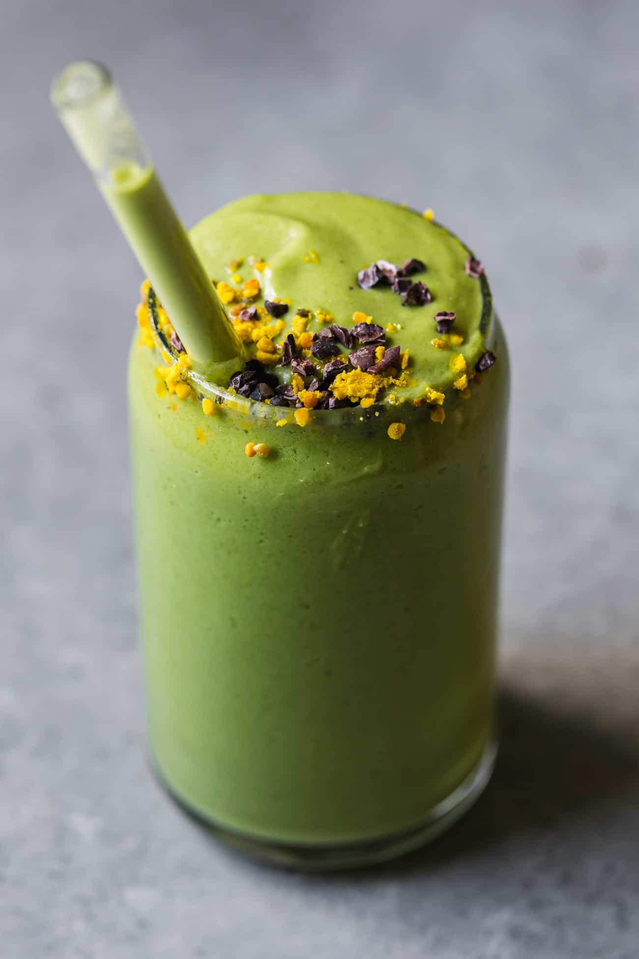 green avocado smoothie with a glass straw and bee pollen on top