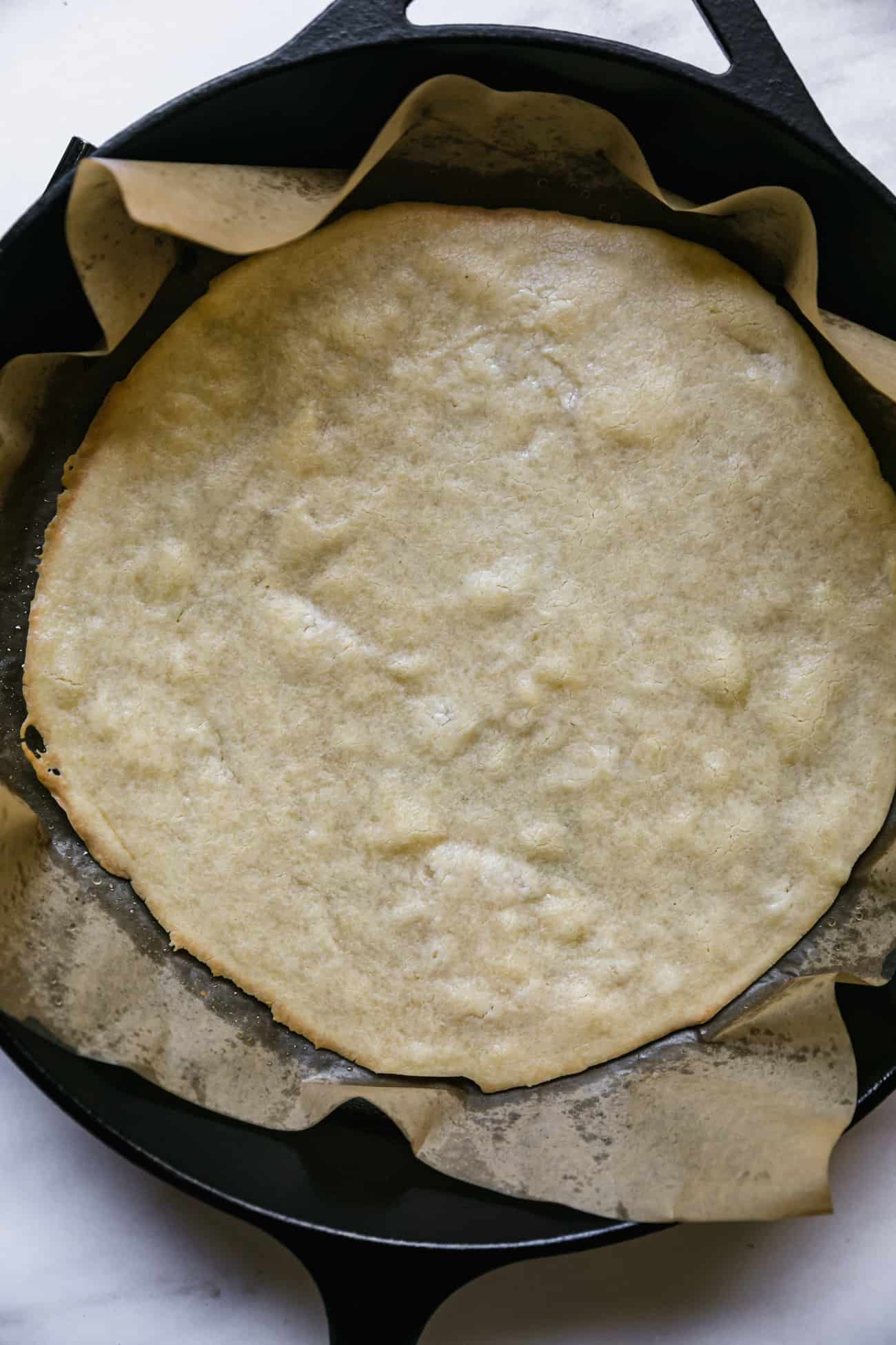 cooked gluten free pizza dough in a cast iron pan with parchment paper
