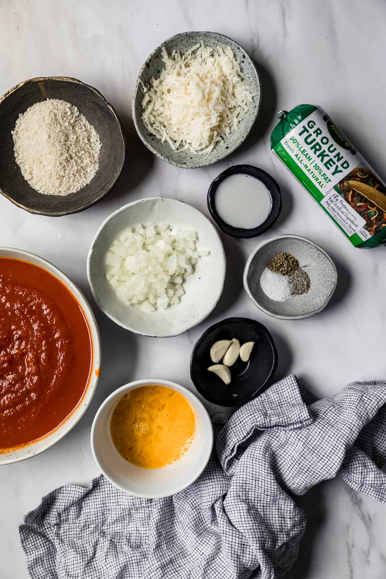 ingredients laid out to make instant pot meatballs: red sauce, eggs, garlic, onion, herbs, parmesan, bread crumbs, milk, and ground turkey.