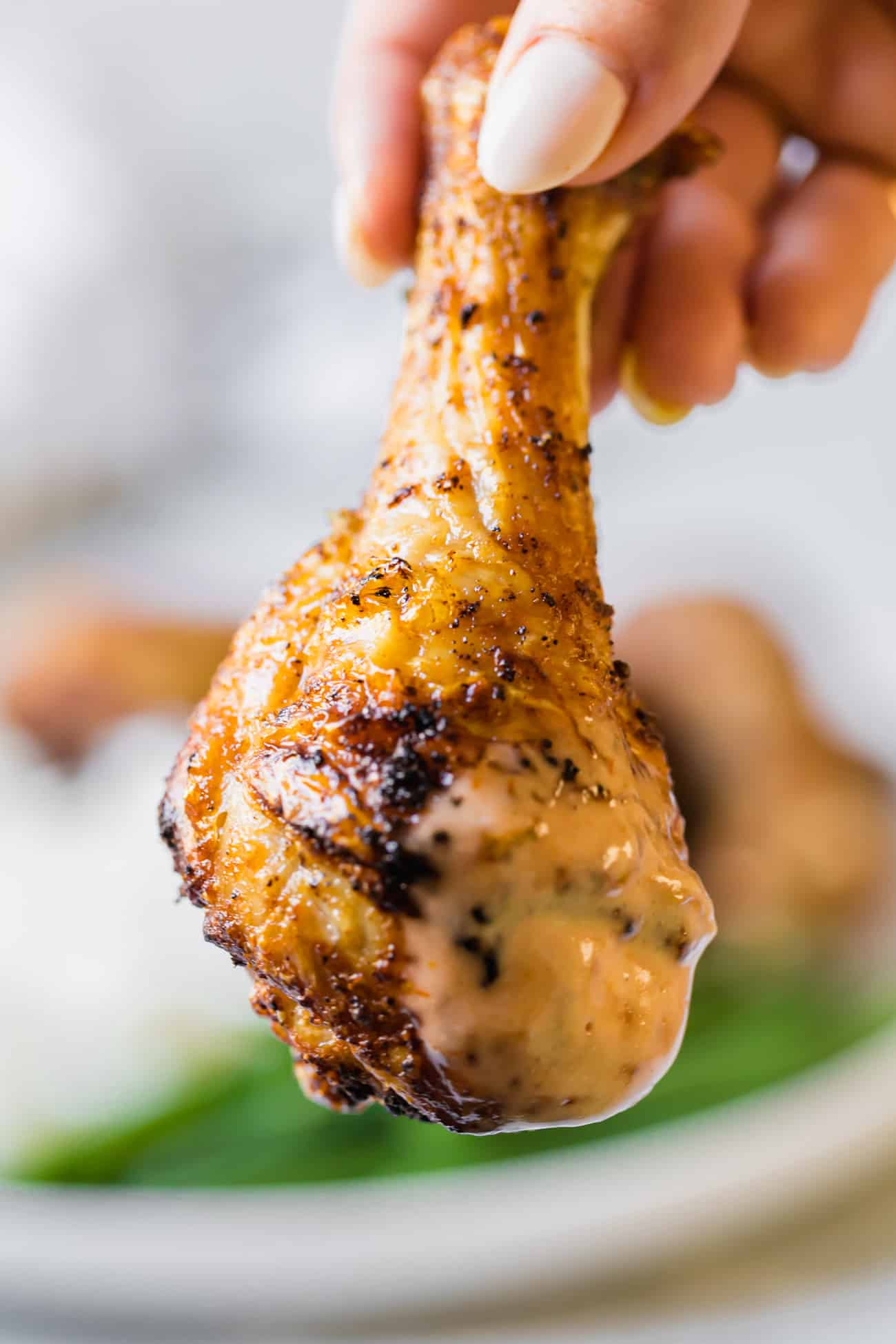 Chicken drumsticks being held dipped in a creamy sauce