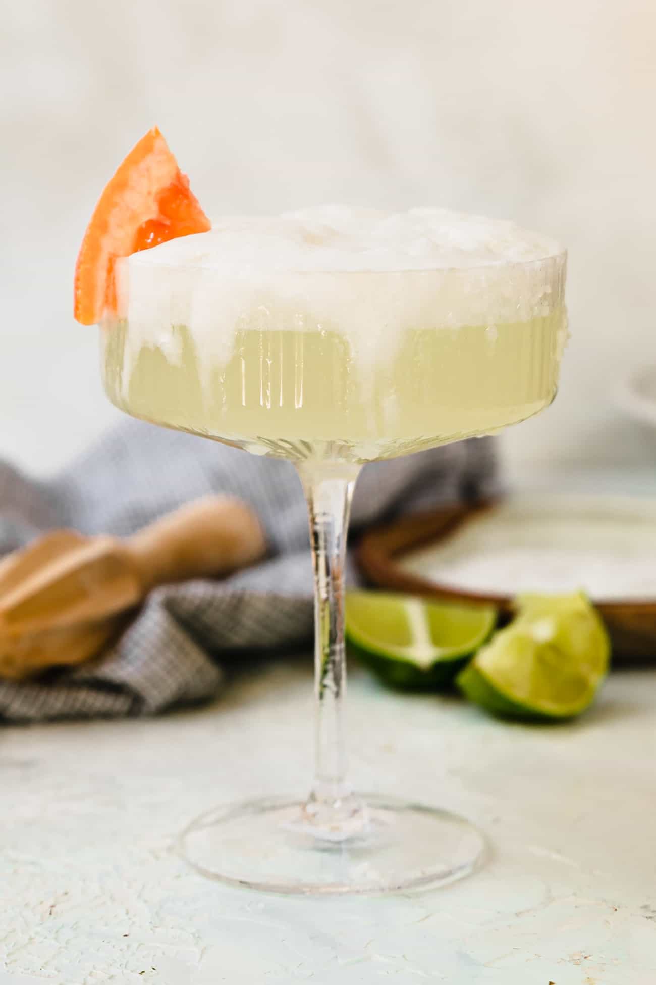 a frothy paloma in a coupe glass with a grapefruit wedge