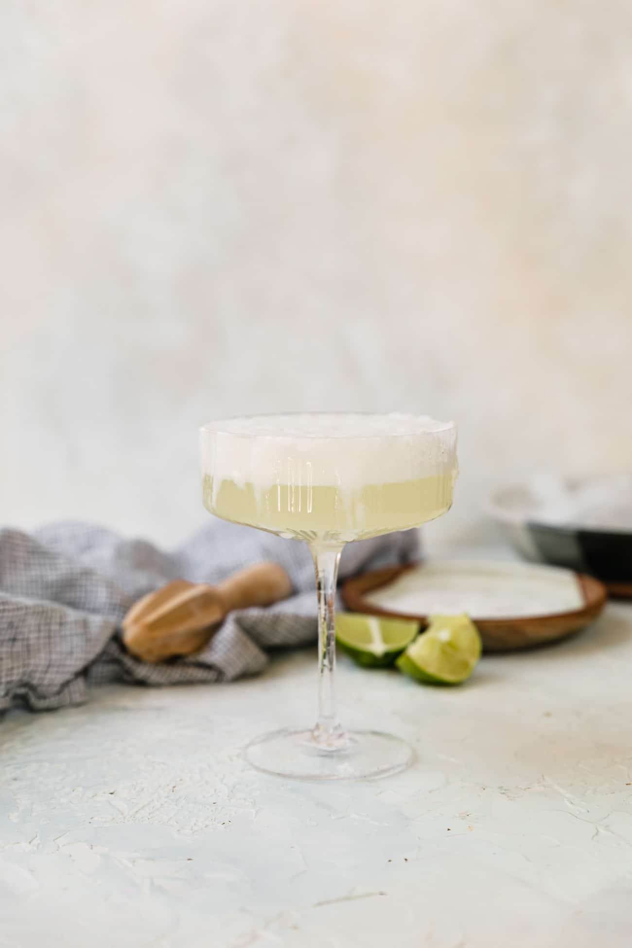 a frothy grapefruit Paloma in a coupe glass with limes on the side