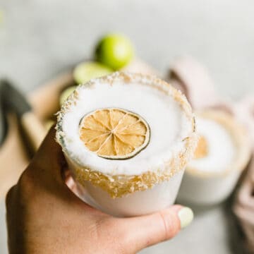 hand holding a frozen coconut margarita with a dehydrated lime on top