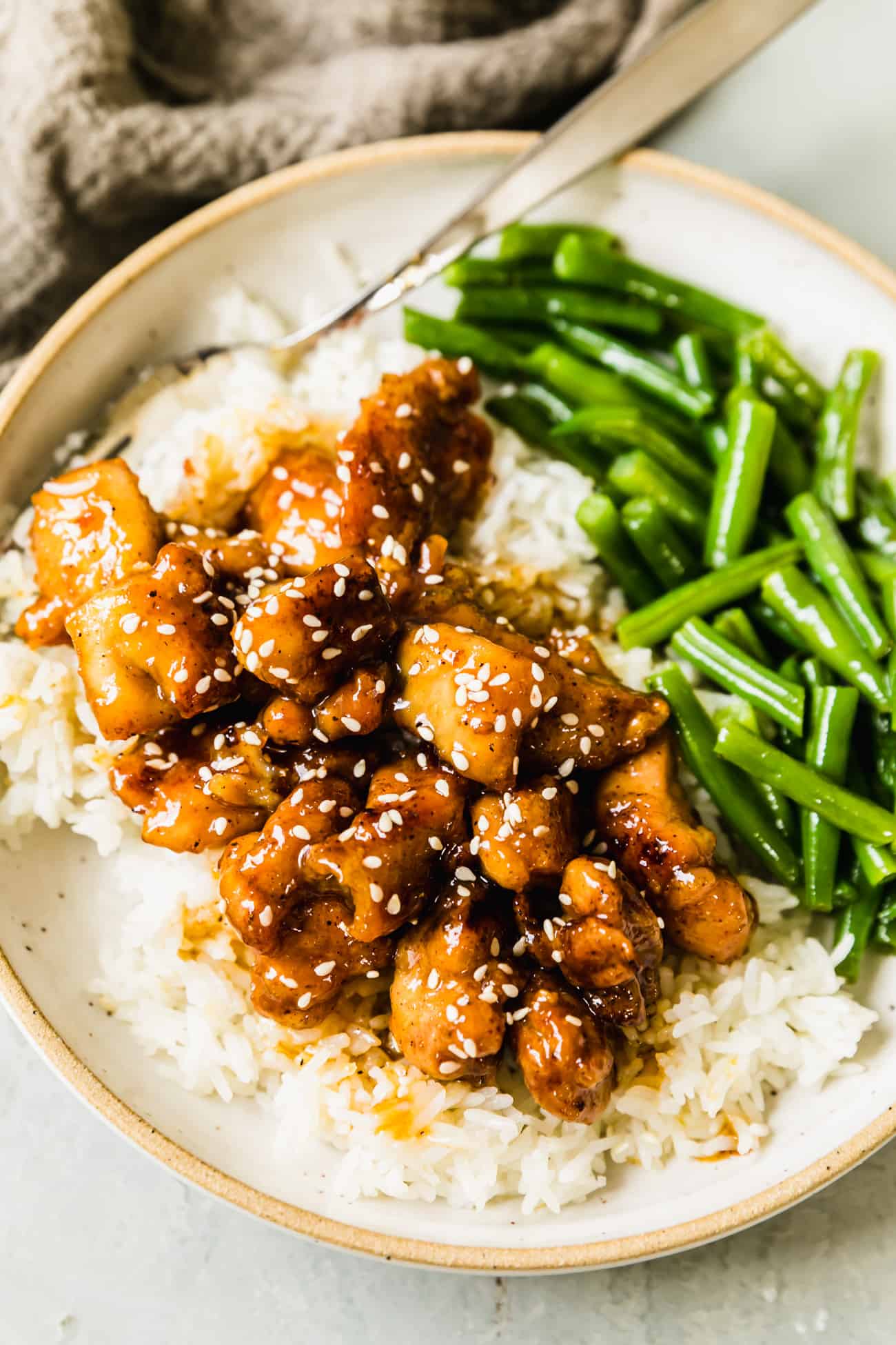 honey chicken on a plate with white rice, green beans, and sesame seeds