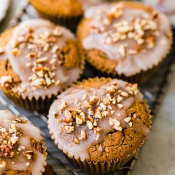 muffins topped off with a white glaze and chopped pecans on a wire rack