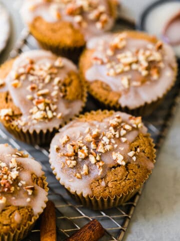 muffins topped off with a white glaze and chopped pecans on a wire rack