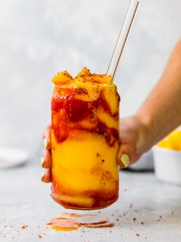 holding a frozen mangonada with a glass straw