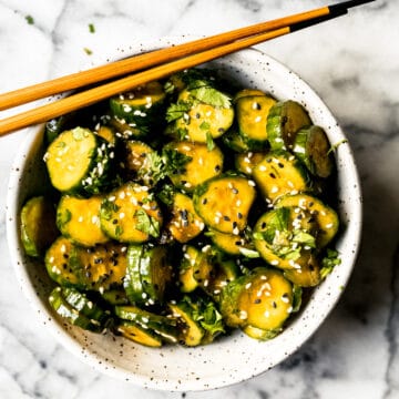 Korean cucumber salad in a ceramic bowl with sesame seeds and wooden chopsticks